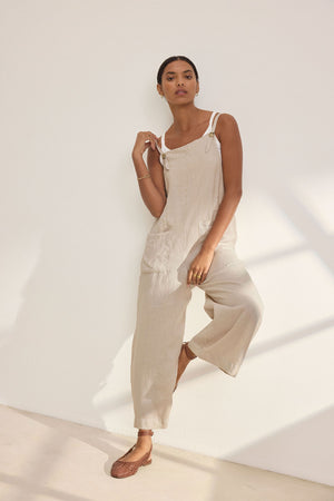 Wearing the ISABEL LINEN ROMPER by Velvet by Graham & Spencer, a person showcases relaxed versatility against a sunlit white wall.
