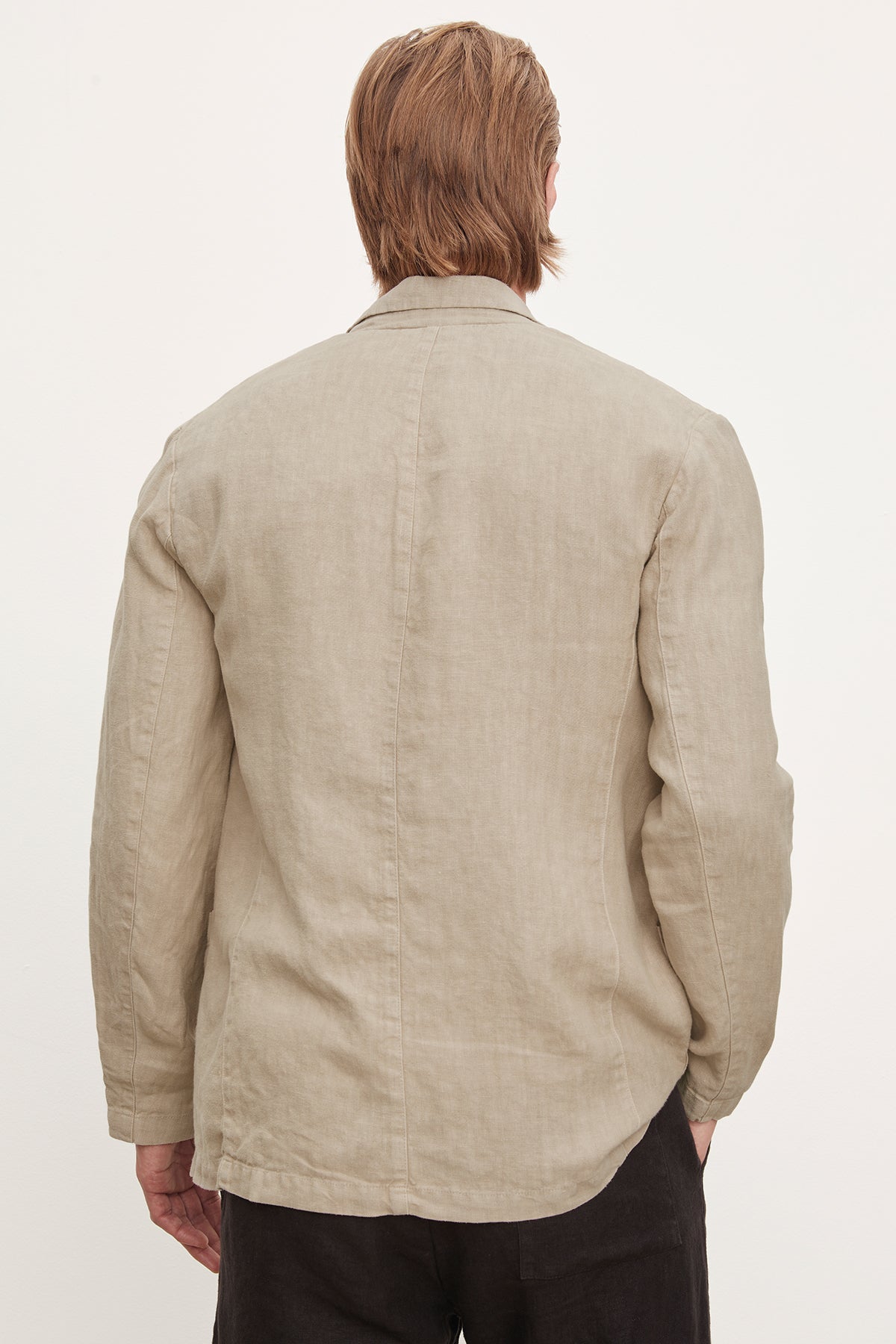   A man viewed from behind, wearing a beige tailored fit linen blazer by Velvet by Graham & Spencer and dark Phelan Linen Pants, standing against a plain white background. 
