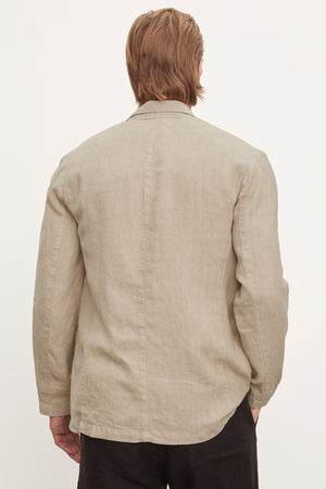 A man viewed from behind, wearing a beige tailored fit linen blazer by Velvet by Graham & Spencer and dark Phelan Linen Pants, standing against a plain white background.