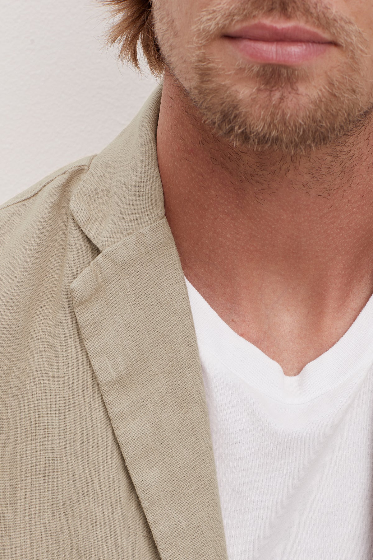   Close-up of a man wearing a Velvet by Graham & Spencer JOSHUA LINEN BLAZER over a white v-neck t-shirt, focusing on the collar area and part of his stubbled chin. 