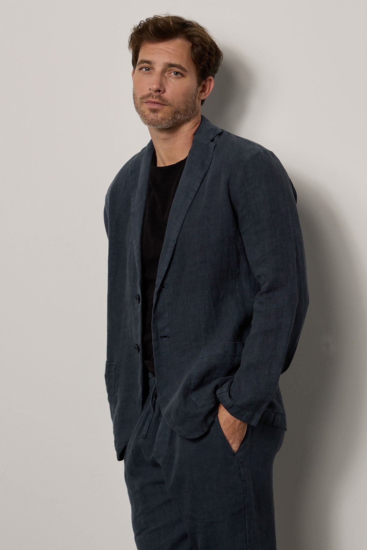 A man in a Velvet by Graham & Spencer Joshua Linen Blazer leaning against a wall.-35678528602305