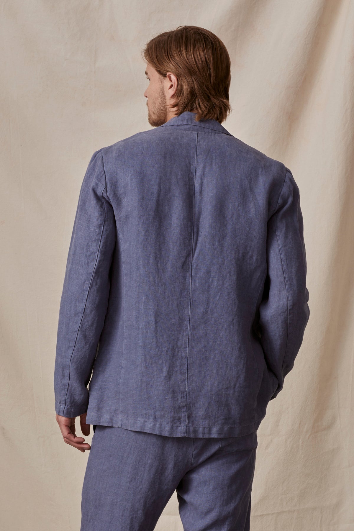 A man viewed from the back wearing a casual blue linen shirt and Phelan Linen Pant against a beige background in the JOSHUA LINEN BLAZER by Velvet by Graham & Spencer.-36805484871873