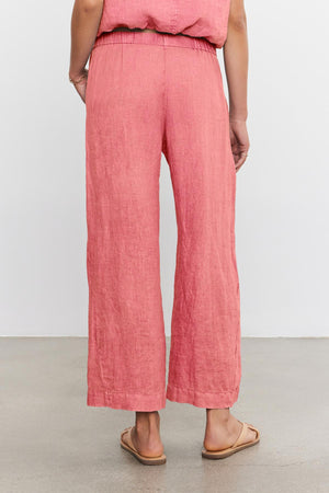A person is standing against a plain white background wearing pink LOLA LINEN PANT by Velvet by Graham & Spencer and tan sandals, with their back facing the camera.