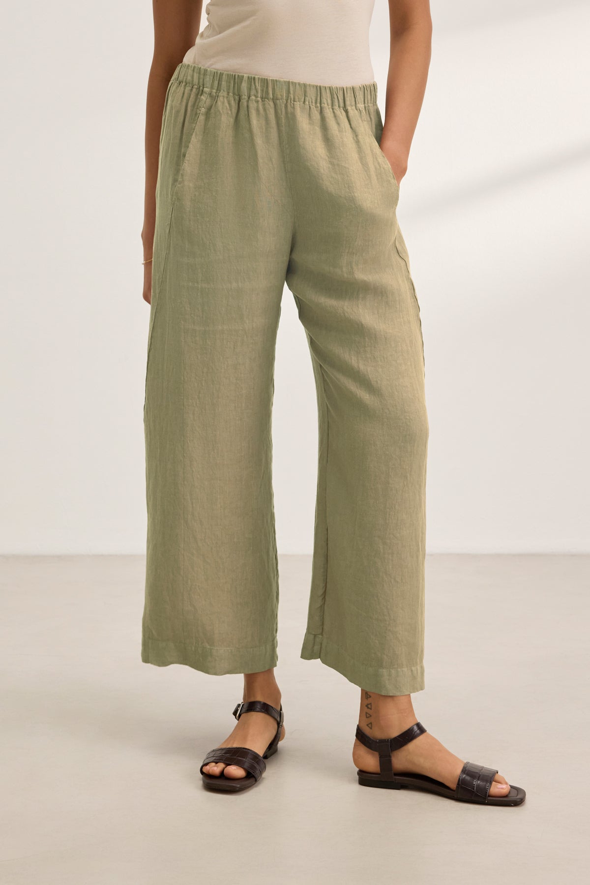 Wearing the Velvet by Graham & Spencer LOLA LINEN PANT, paired with a beige top and black sandals, a person stands on a light-colored floor against a plain background.-39359713083585
