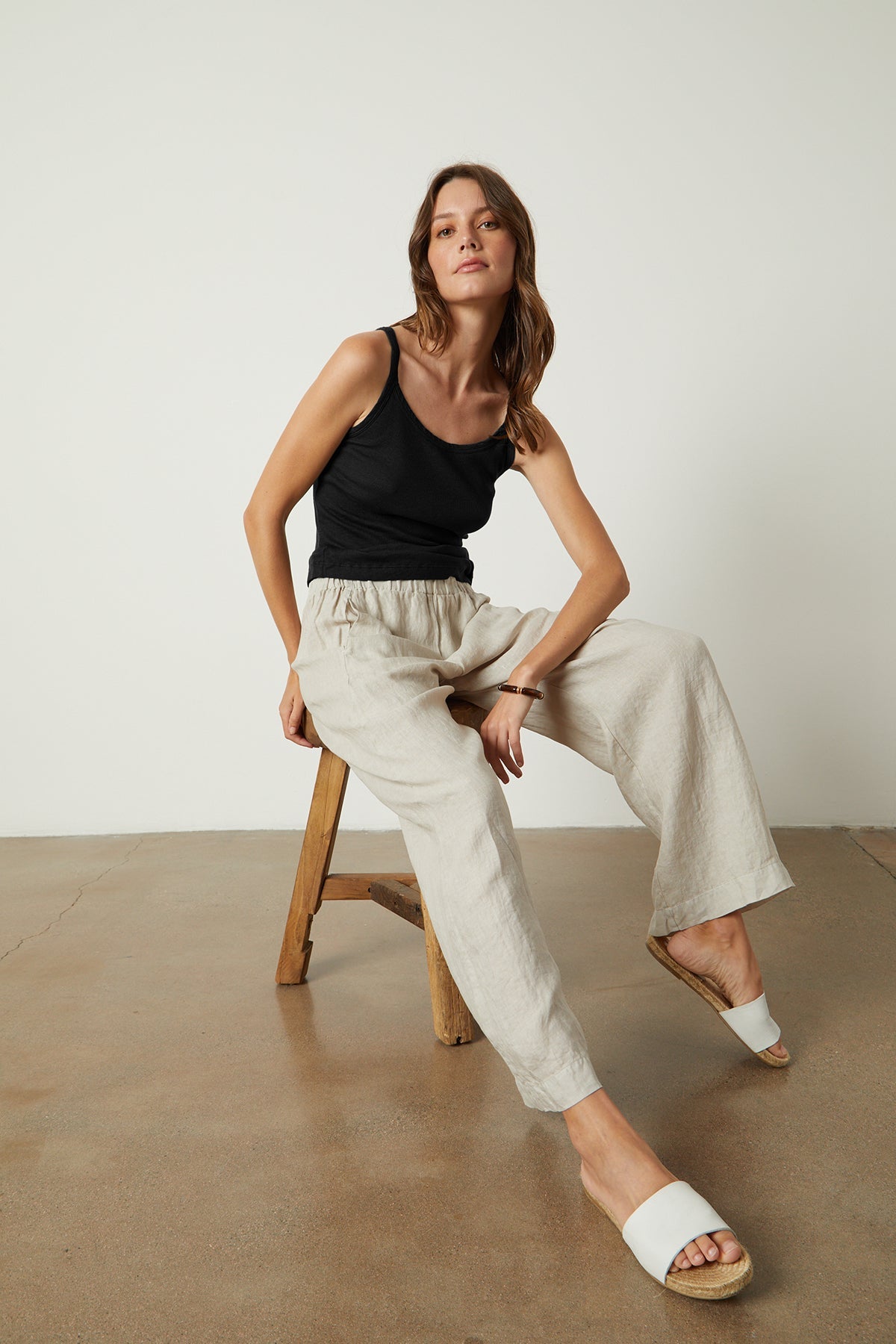 A woman is sitting on a stool in a Velvet by Graham & Spencer ALIZA RIBBED COTTON LAYERING TANK and linen pants.-35206750830785