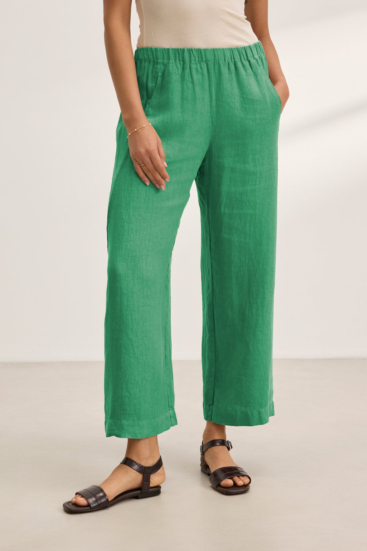 Wearing the LOLA LINEN PANT by Velvet by Graham & Spencer in green, styled with a sleeveless beige top, black sandals, and a bracelet. Relaxed leg fit, hands in pockets, posed against a plain light background.-39333752537281