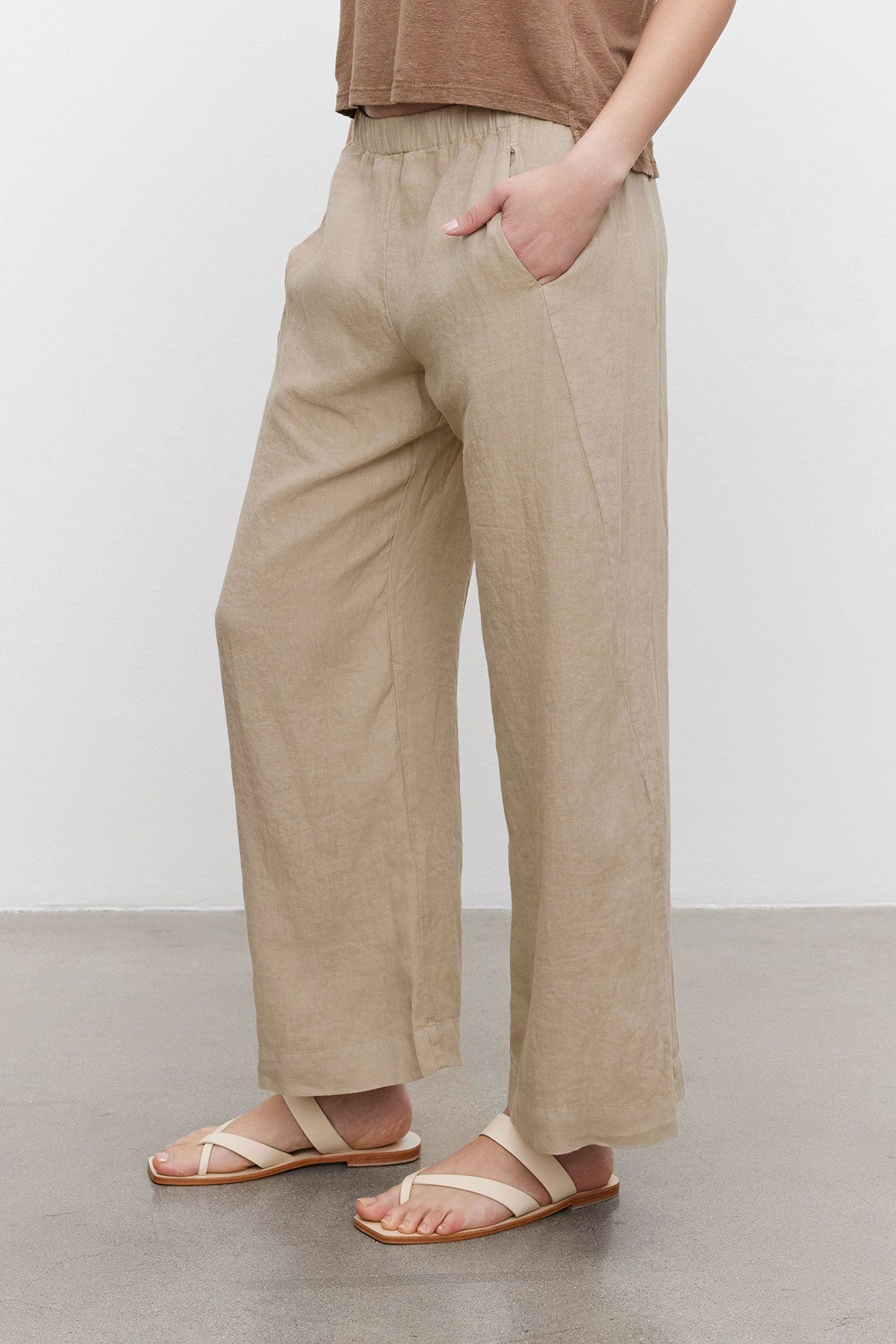   Person standing in a neutral pose wearing Velvet by Graham & Spencer's LOLA LINEN PANT and white sandals on a plain background. 