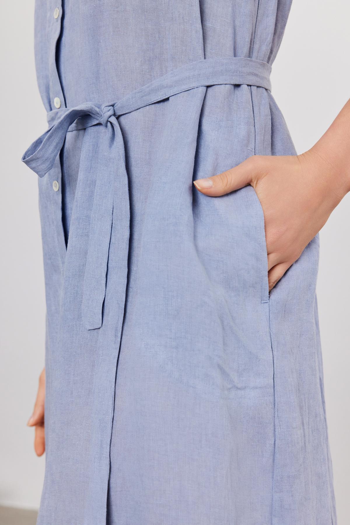   Close-up of a person wearing a Velvet by Graham & Spencer LUNA LINEN DRESS with a tied waist belt, hand placed in the side pocket. 