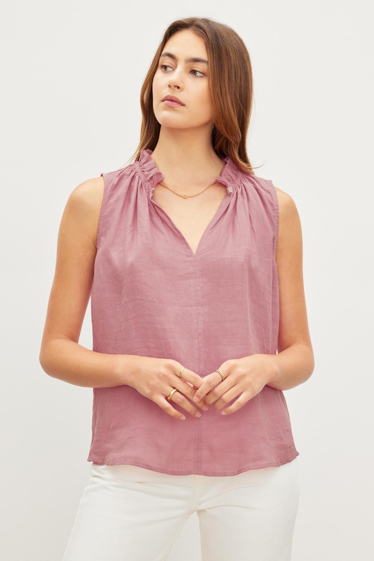 Woman in a pink MASIE LINEN TANK TOP from Velvet by Graham & Spencer and white pants, standing against a plain background, looking to the side with a serene expression.-36571197374657