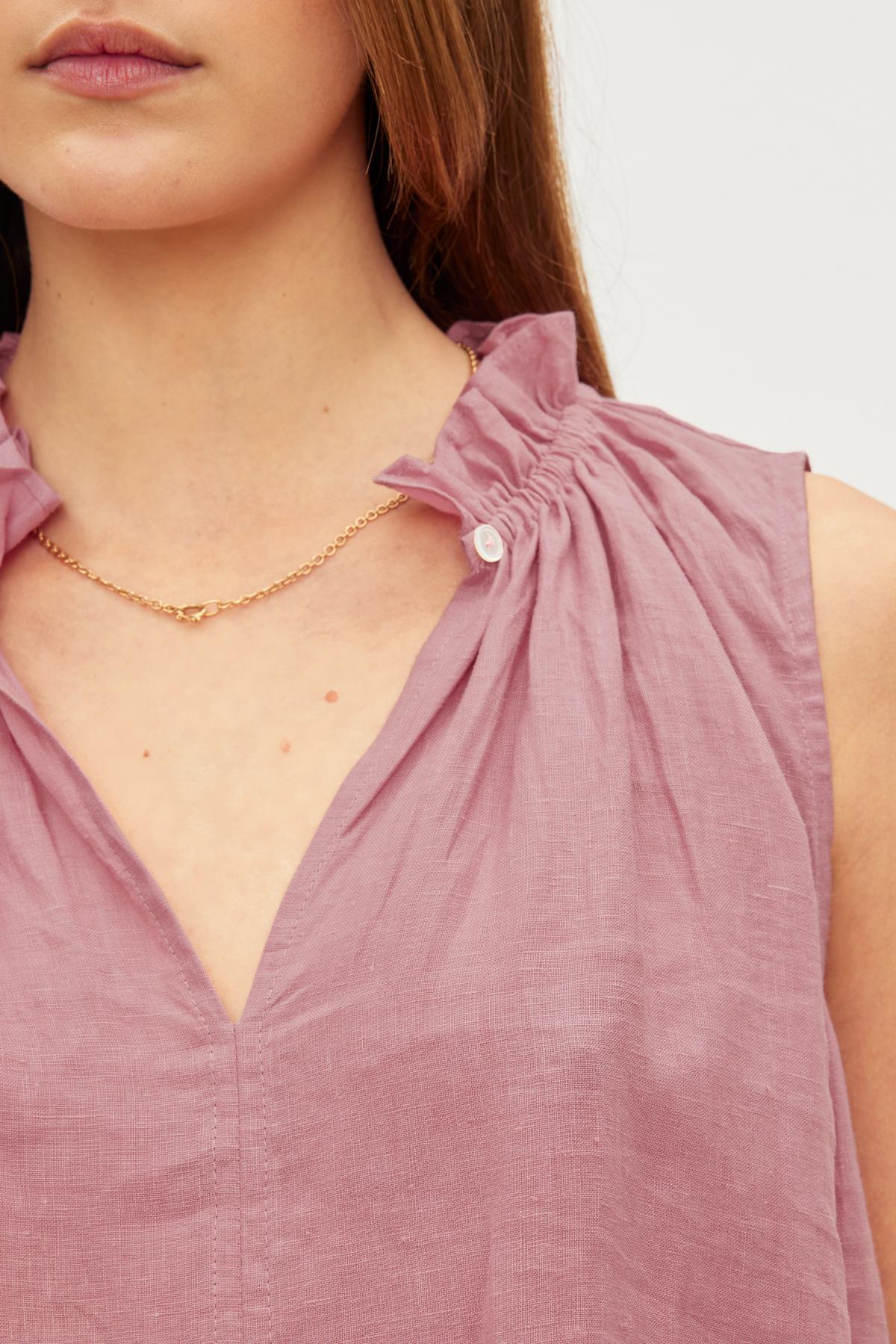  Close-up of a woman wearing a MASIE LINEN TANK TOP from Velvet by Graham & Spencer, with an elastic ruffle neckline and a delicate gold chain necklace with a small pendant. 