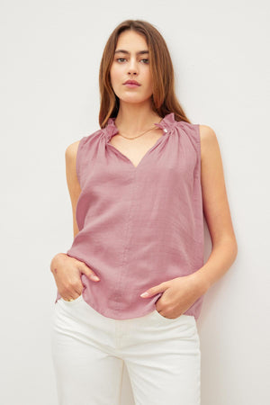 Woman in a pink Velvet by Graham & Spencer MASIE LINEN TANK TOP and white pants standing against a white background, hands in pockets, looking at the camera.