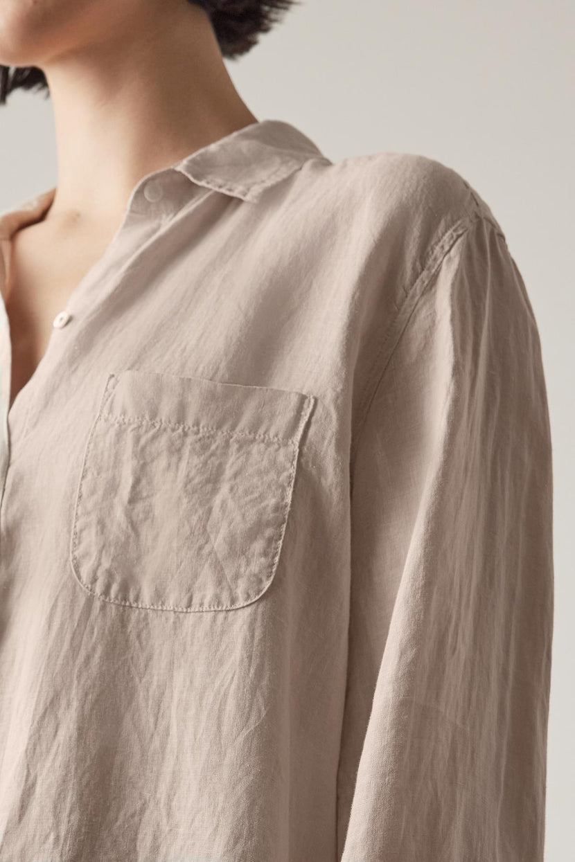 Close-up of a person wearing a light-colored, rumpled MULHOLLAND LINEN SHIRT by Velvet by Jenny Graham with a front pocket, showcasing the relaxed silhouette of the upper torso and partial neck.