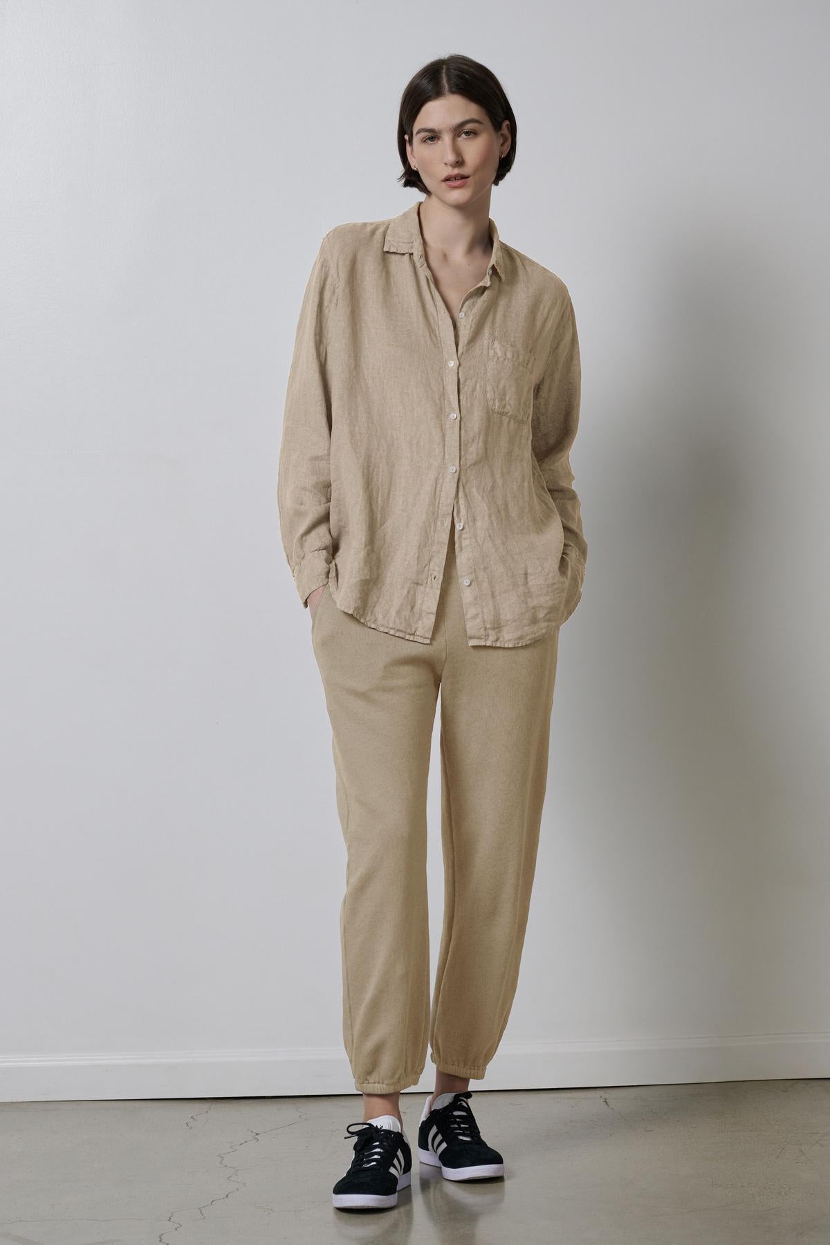   Woman dressed in a casual beige linen shirt and ZUMA SWEATPANT by Velvet by Jenny Graham with black sneakers standing against a plain background. 