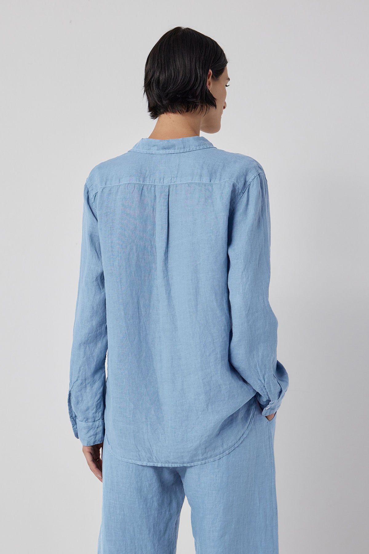   The woman is seen from the back in a blue linen Mulholland shirt and pants, showcasing a relaxed silhouette by Velvet by Jenny Graham. 
