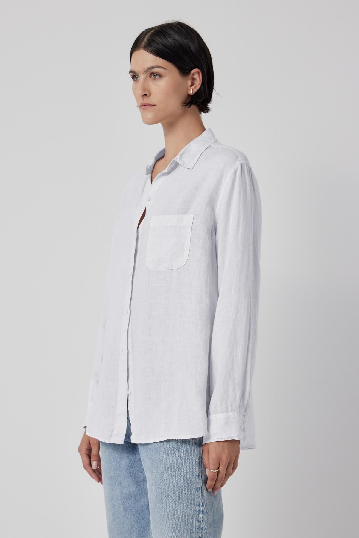   Woman wearing a Velvet by Jenny Graham Mulholland Shirt, a relaxed silhouette, casual white linen button-up shirt with a chest pocket, paired with denim jeans, against a neutral background. 