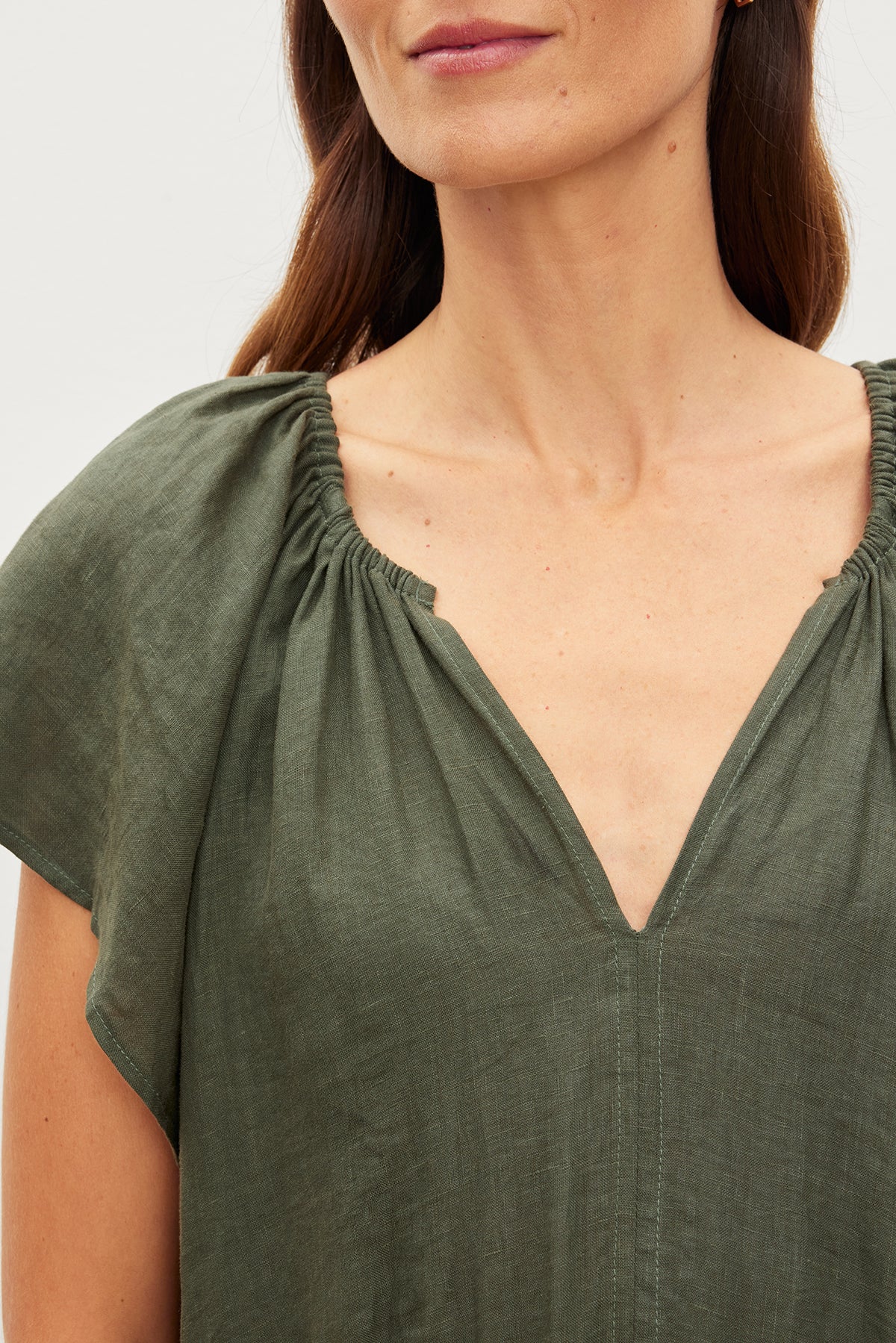 Close-up of a woman in a green woven linen dress with a v-neckline; only her neck and shoulders are visible, wearing the Velvet by Graham & Spencer PEPPER LINEN V-NECK DRESS.-35967692112065
