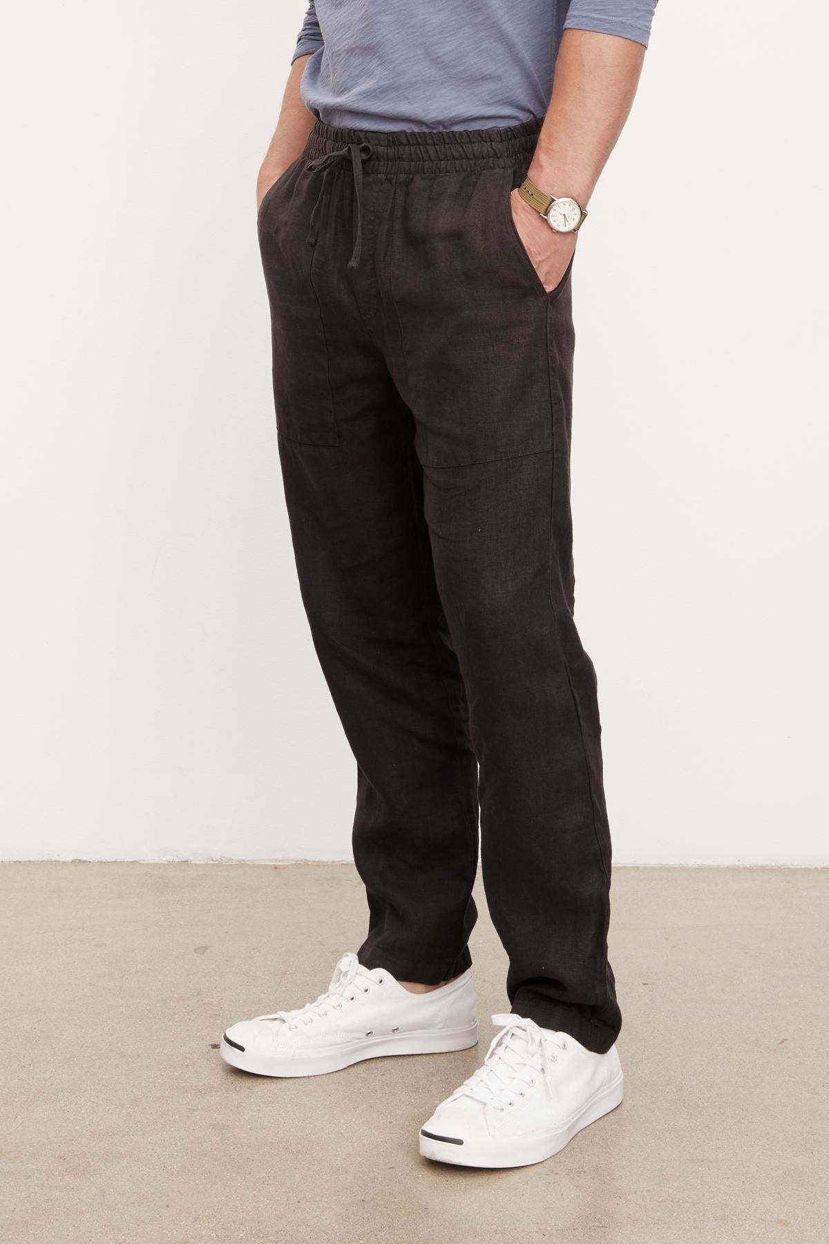 A person wearing Velvet by Graham & Spencer black Phelan linen pants and white shoes.-36009949495489