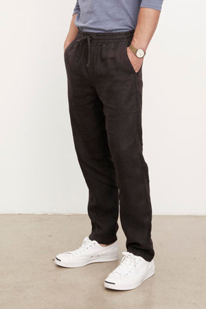 A person wearing Velvet by Graham & Spencer black Phelan linen pants and white shoes.