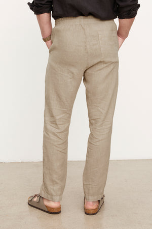 Rear view of a person standing in Velvet by Graham & Spencer's Phelan Linen Pant and brown sandals against a white background.