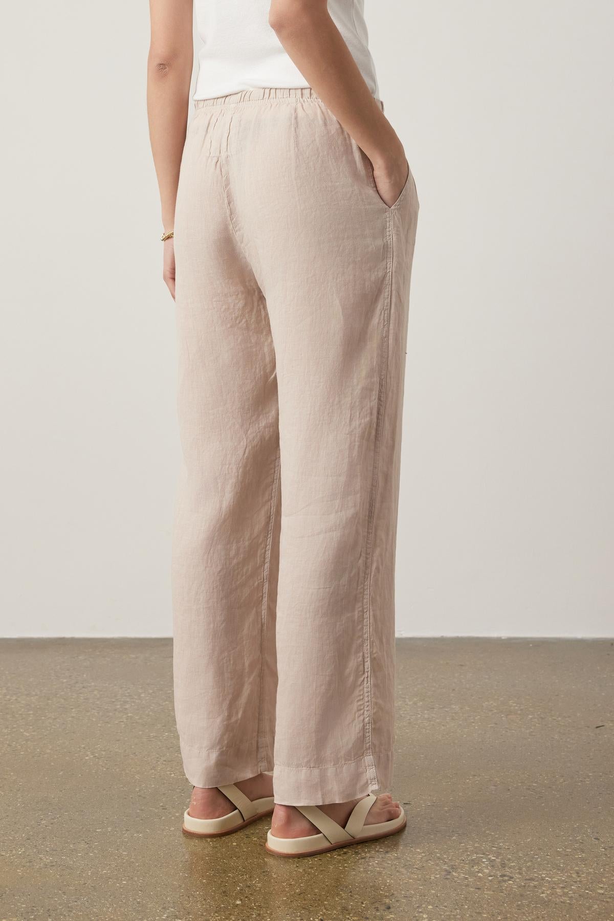   Woman in beige Velvet by Jenny Graham PICO LINEN PANT and white sandals, standing with back to the camera, focusing on the clothing fit and texture. 