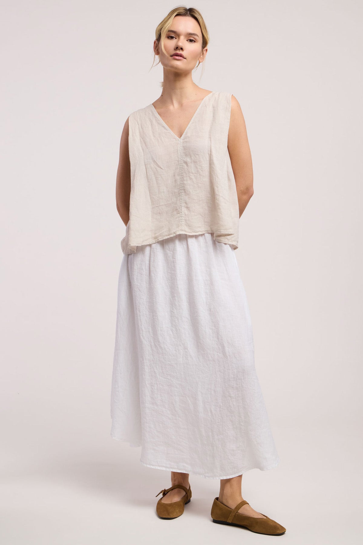 Wearing the RENNA LINEN TOP by Velvet by Graham & Spencer, a long white skirt, and brown flats, someone stands against a light backdrop—capturing the essence of effortless summer style.
