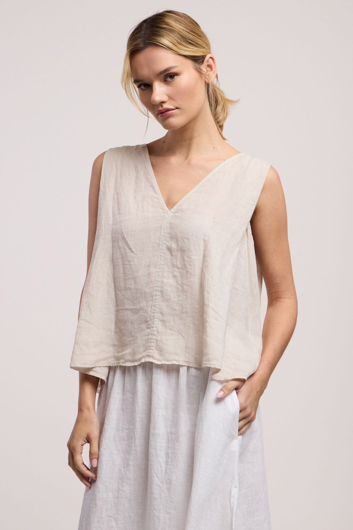 A person wearing the RENNA LINEN TOP by Velvet by Graham & Spencer, paired with a white skirt, stands against a plain light background.