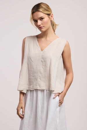 A person wearing the RENNA LINEN TOP by Velvet by Graham & Spencer, paired with a white skirt, stands against a plain light background.