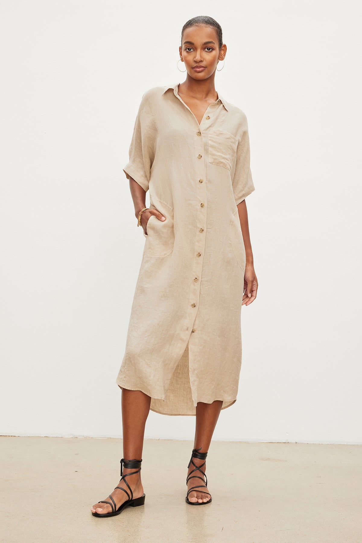 A woman stands against a plain background wearing the Sandra Linen Dress by Velvet by Graham & Spencer, featuring short sleeves, a detachable belt, and sandals.-35967717474497