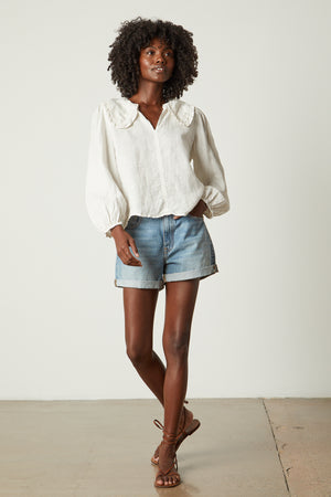 The model is wearing a Velvet by Graham & Spencer Sofia Linen Top and denim shorts.