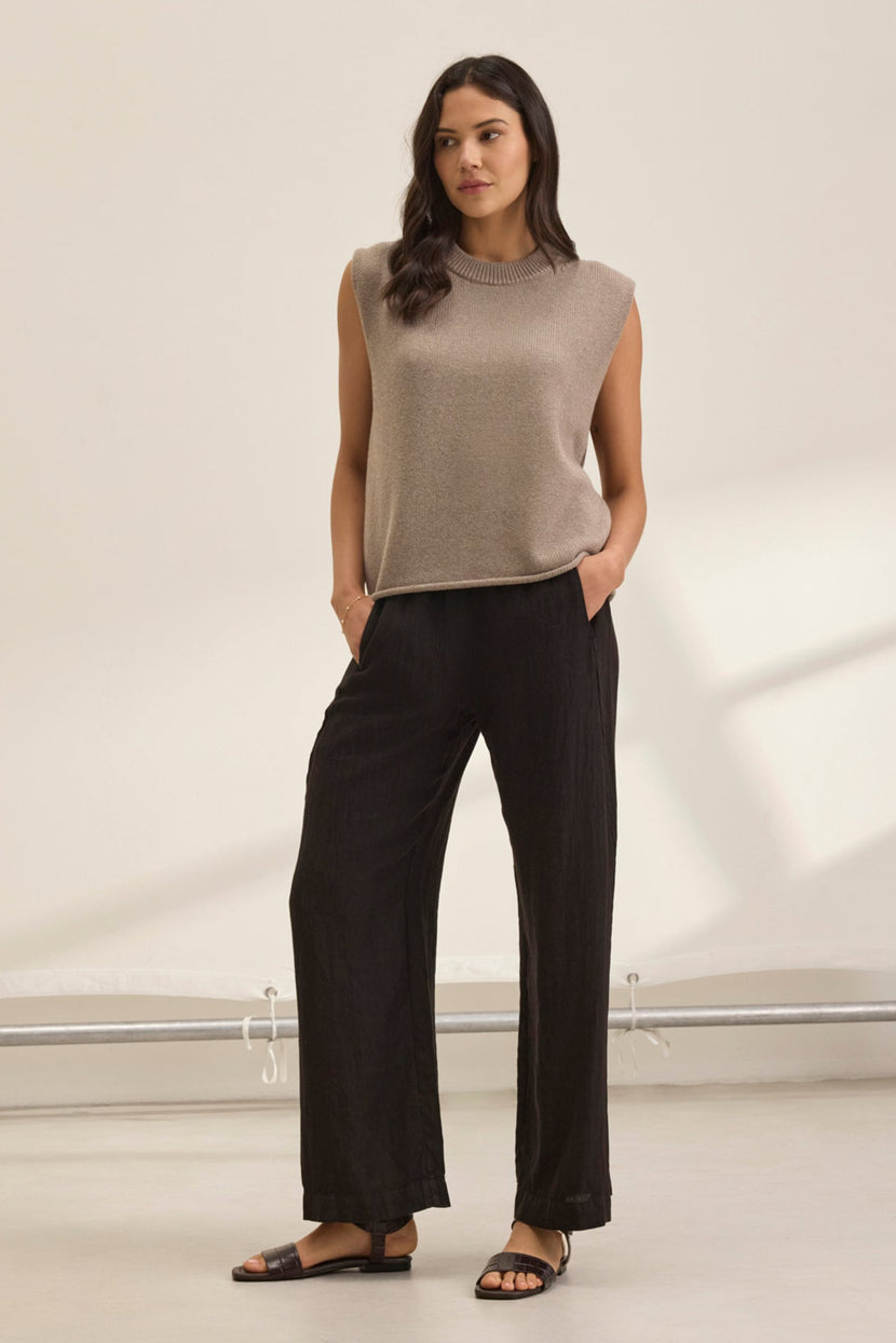 A person wearing the STEPHANIE LINEN PANT from Velvet by Graham & Spencer with a beige sleeveless top, stands with hands in pockets against a light background.