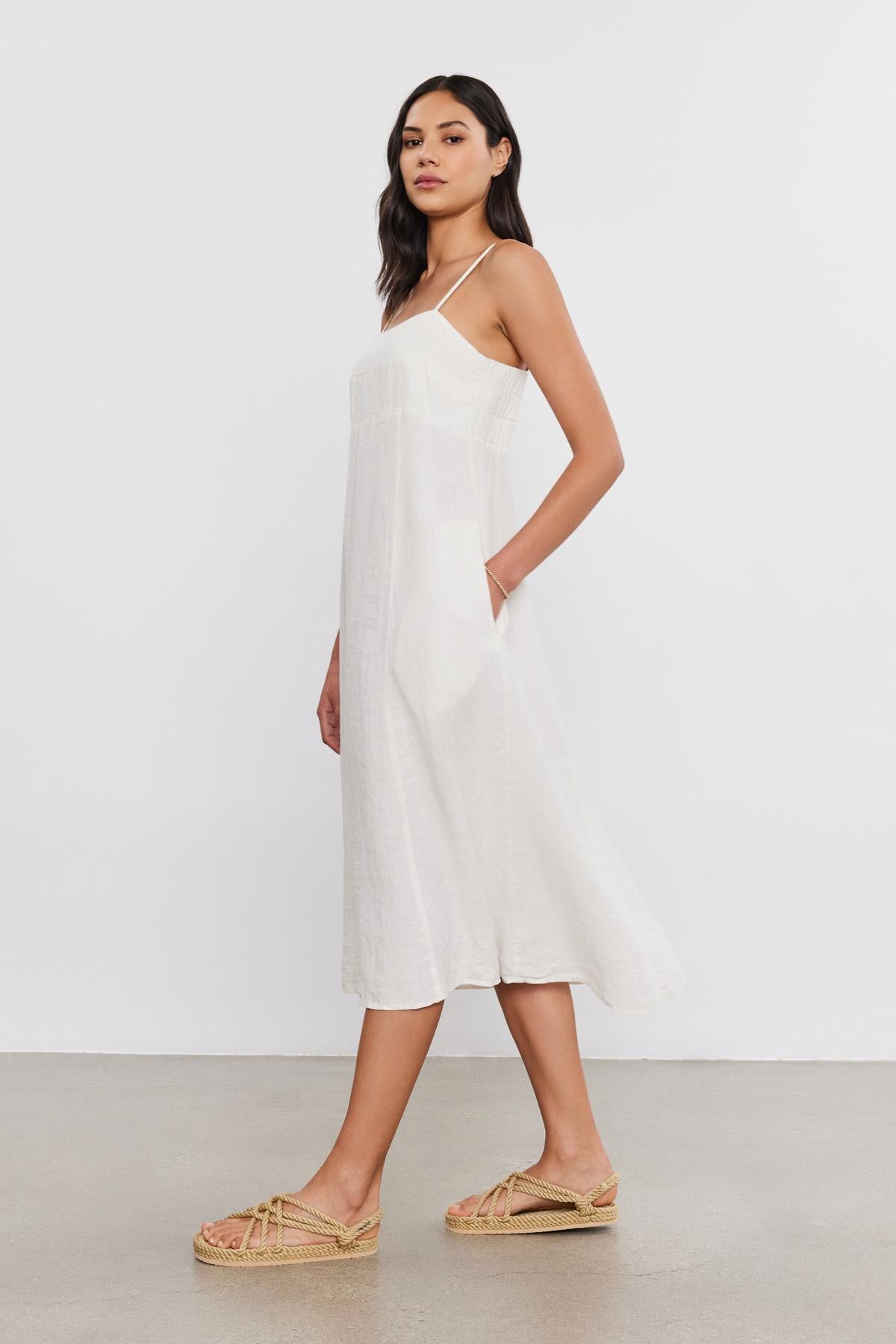   Woman wearing a sleeveless white midi dress (Stephie Linen Dress by Velvet by Graham & Spencer) and matching espadrilles, standing in a studio with a neutral background. 