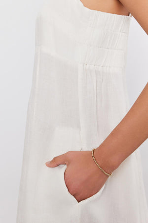 Close-up of a woman's side, wearing a white sleeveless STEPHIE LINEN DRESS with pleated details, focusing on her hand adorned with a gold bracelet by Velvet by Graham & Spencer.