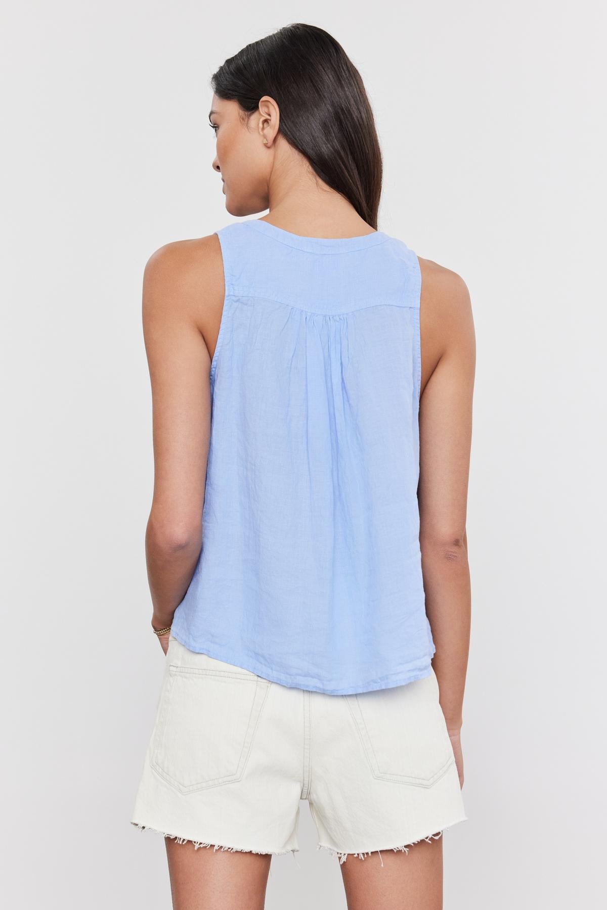 A woman with her back to the camera, wearing a Velvet by Graham & Spencer TACY LINEN TANK TOP in light blue and white shorts, standing against a plain background.-36752965468353