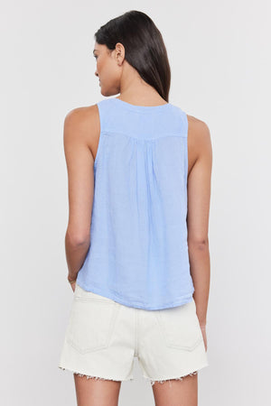 A woman with her back to the camera, wearing a Velvet by Graham & Spencer TACY LINEN TANK TOP in light blue and white shorts, standing against a plain background.