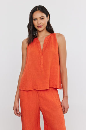 A woman stands against a plain background, wearing a sleeveless orange TACY LINEN TANK TOP with a high-low scooped hemline and matching pants, looking at the camera by Velvet by Graham & Spencer.