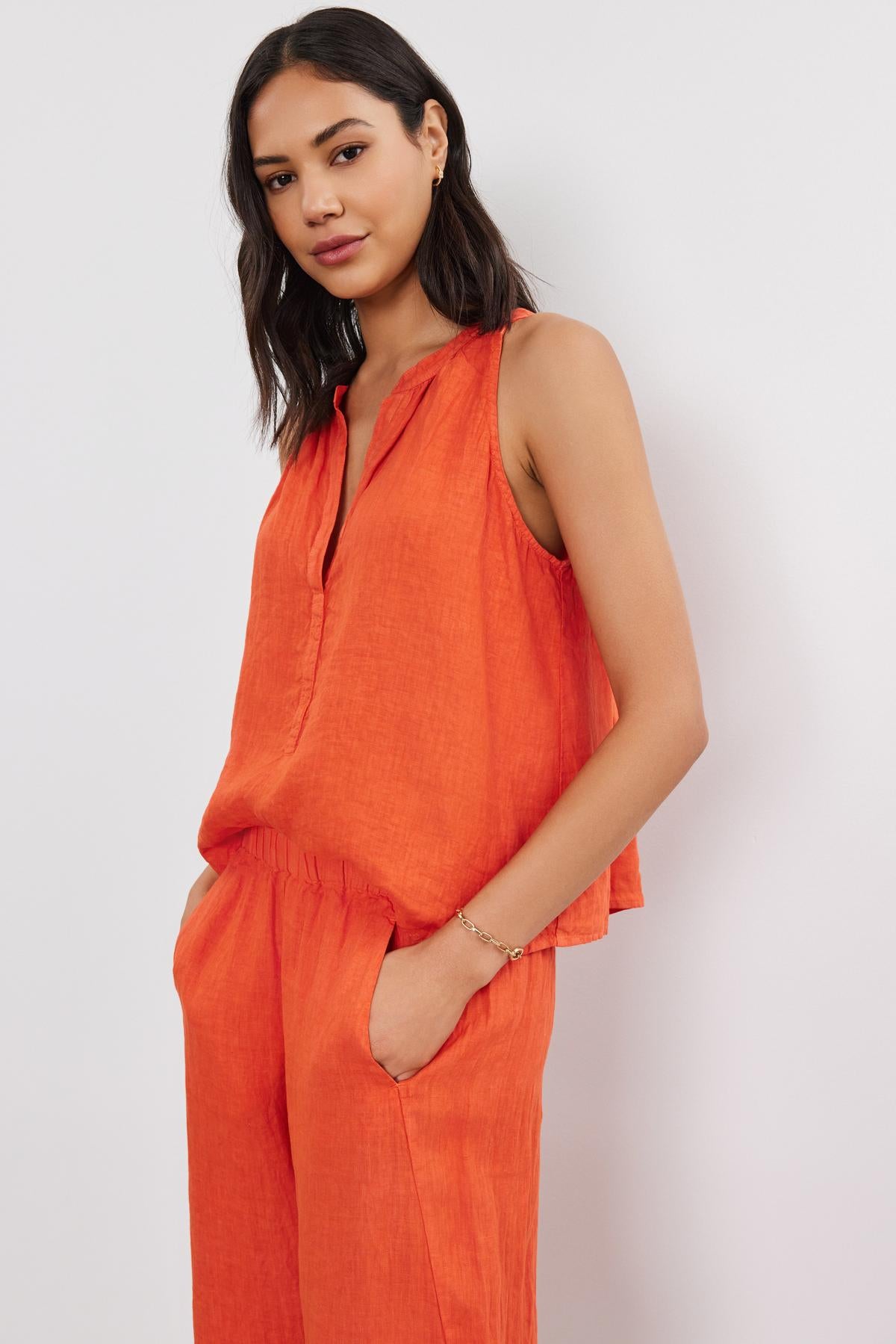   A woman in a Velvet by Graham & Spencer TACY LINEN TANK TOP with a high-low scooped hemline stands against a plain background, slightly smiling at the camera. 