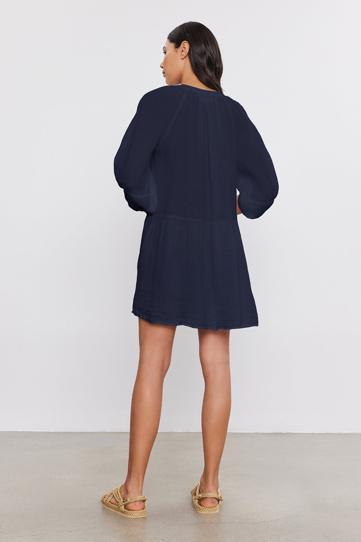   Woman standing with her back to the camera, wearing a Velvet by Graham & Spencer VONNIE LINEN DRESS and gold espadrilles, against a neutral background. 