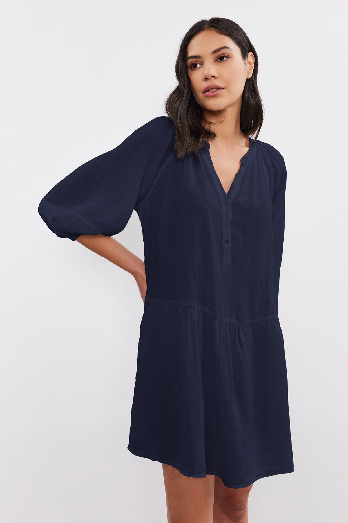   A woman wearing a navy blue VONNIE LINEN DRESS by Velvet by Graham & Spencer, with three-quarter puff sleeves, standing with one hand on her hip. 