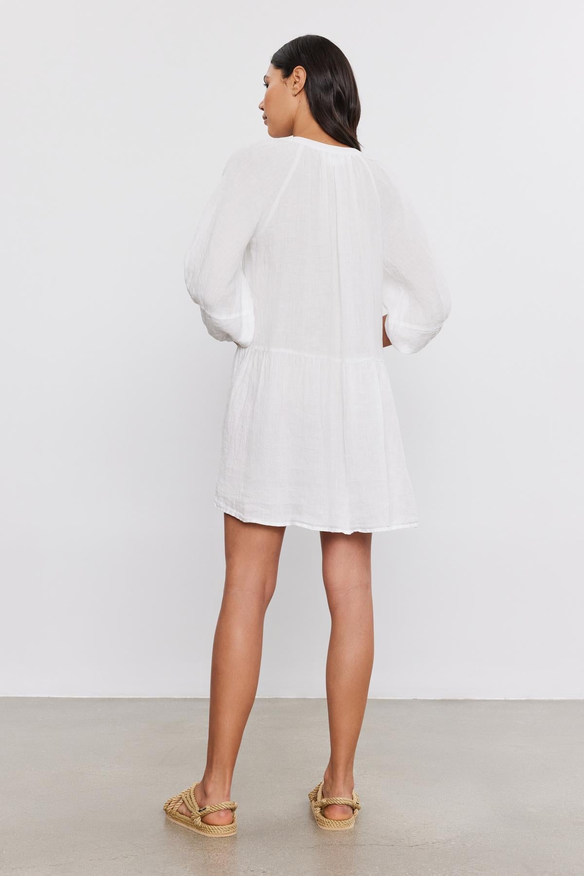 A woman stands with her back facing the camera, wearing a VONNIE LINEN DRESS by Velvet by Graham & Spencer with puff sleeves and gold espadrilles, against a plain gray background.-36910023016641