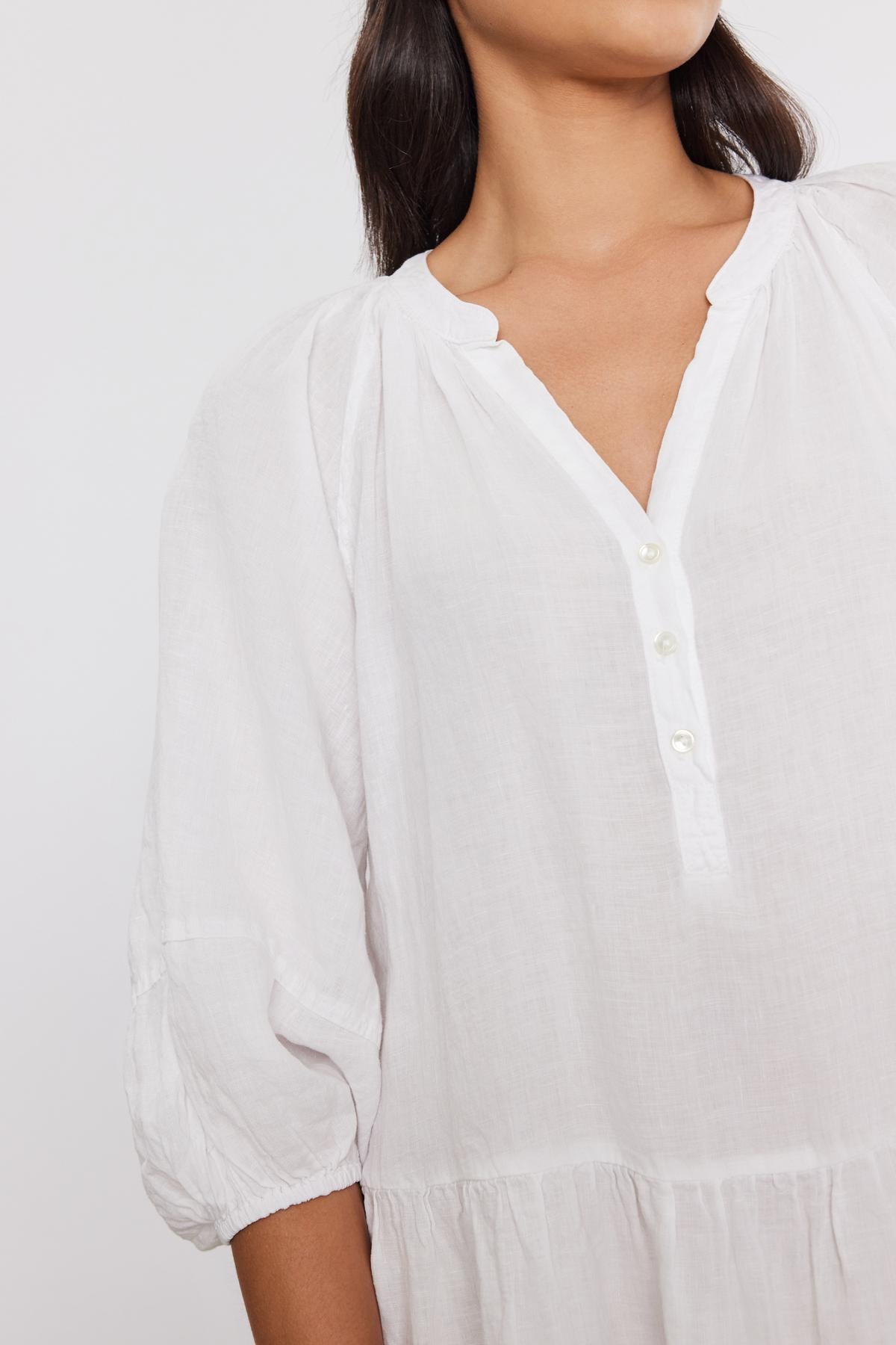   Close-up of a woman wearing a Velvet by Graham & Spencer VONNIE LINEN DRESS with puff sleeves and a buttoned neckline, focusing on the collar and upper chest area. 