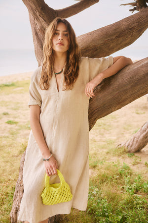 a woman in a Velvet by Graham & Spencer Winley Linen Dress is posing next to a tree holding the Bennie bag in lemon yellow