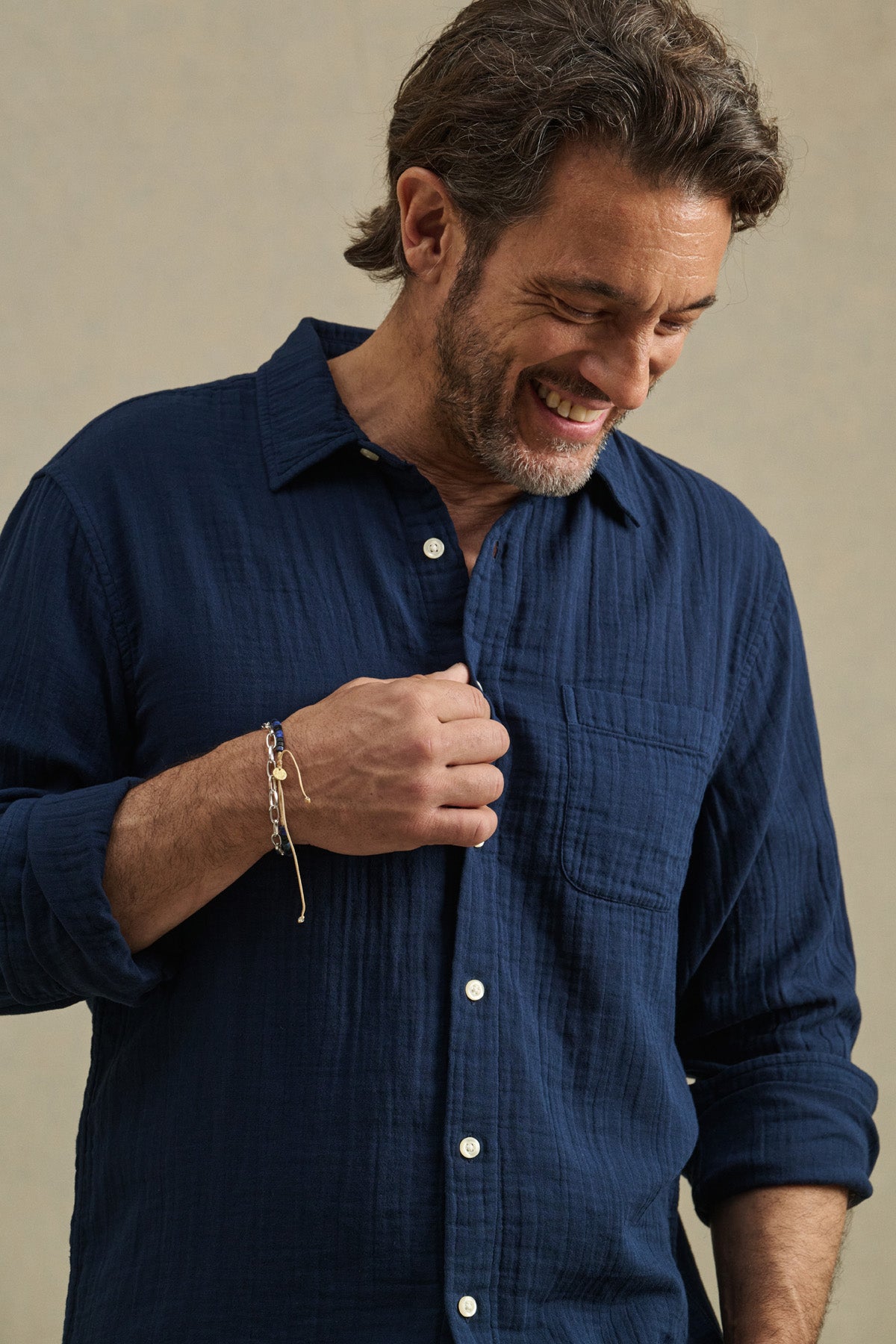 A man with short brown hair and a beard smiles and looks down while holding the placket of the APOLLO SHIRT by Velvet by Graham & Spencer, a navy relaxed button-up featuring a classic collar.-41145204506817