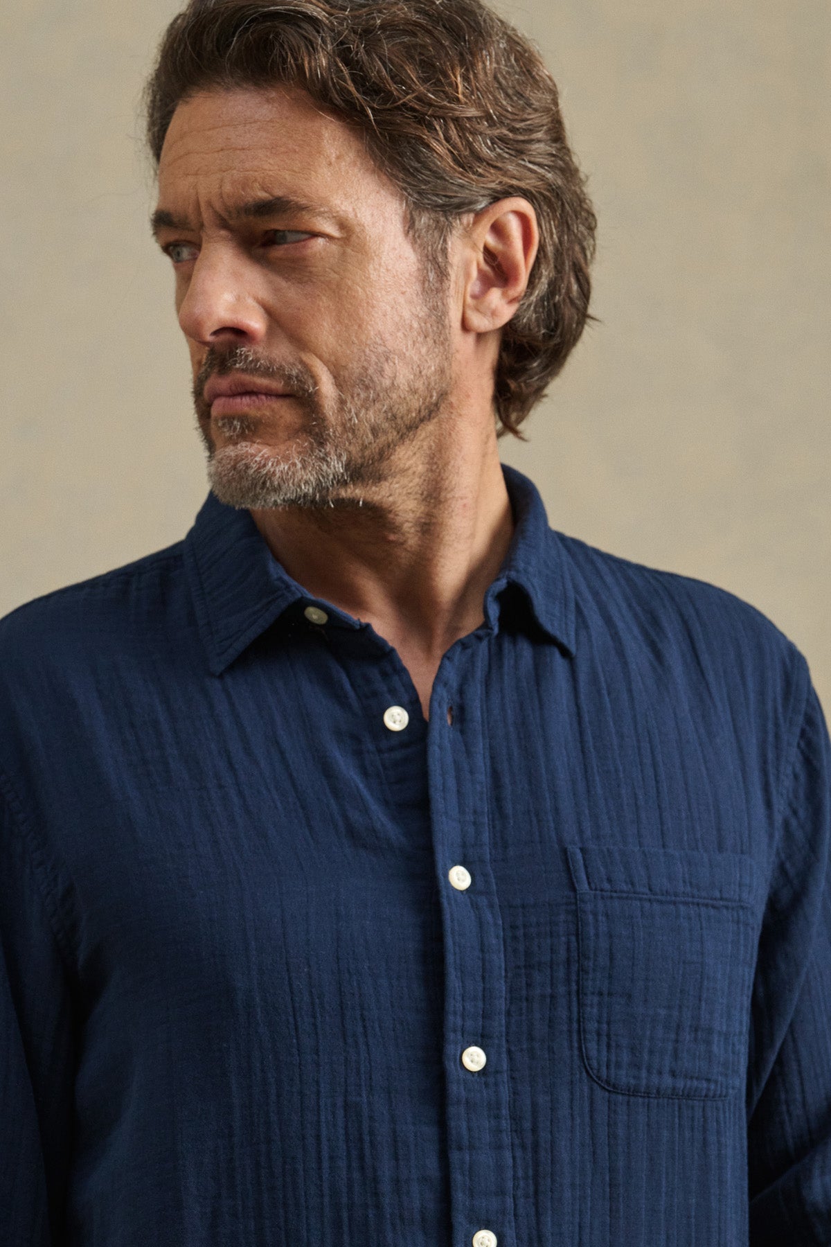 A man with wavy brown hair and a beard wears the APOLLO SHIRT in navy blue by Velvet by Graham & Spencer, looking to his left against a neutral background.-41145204474049