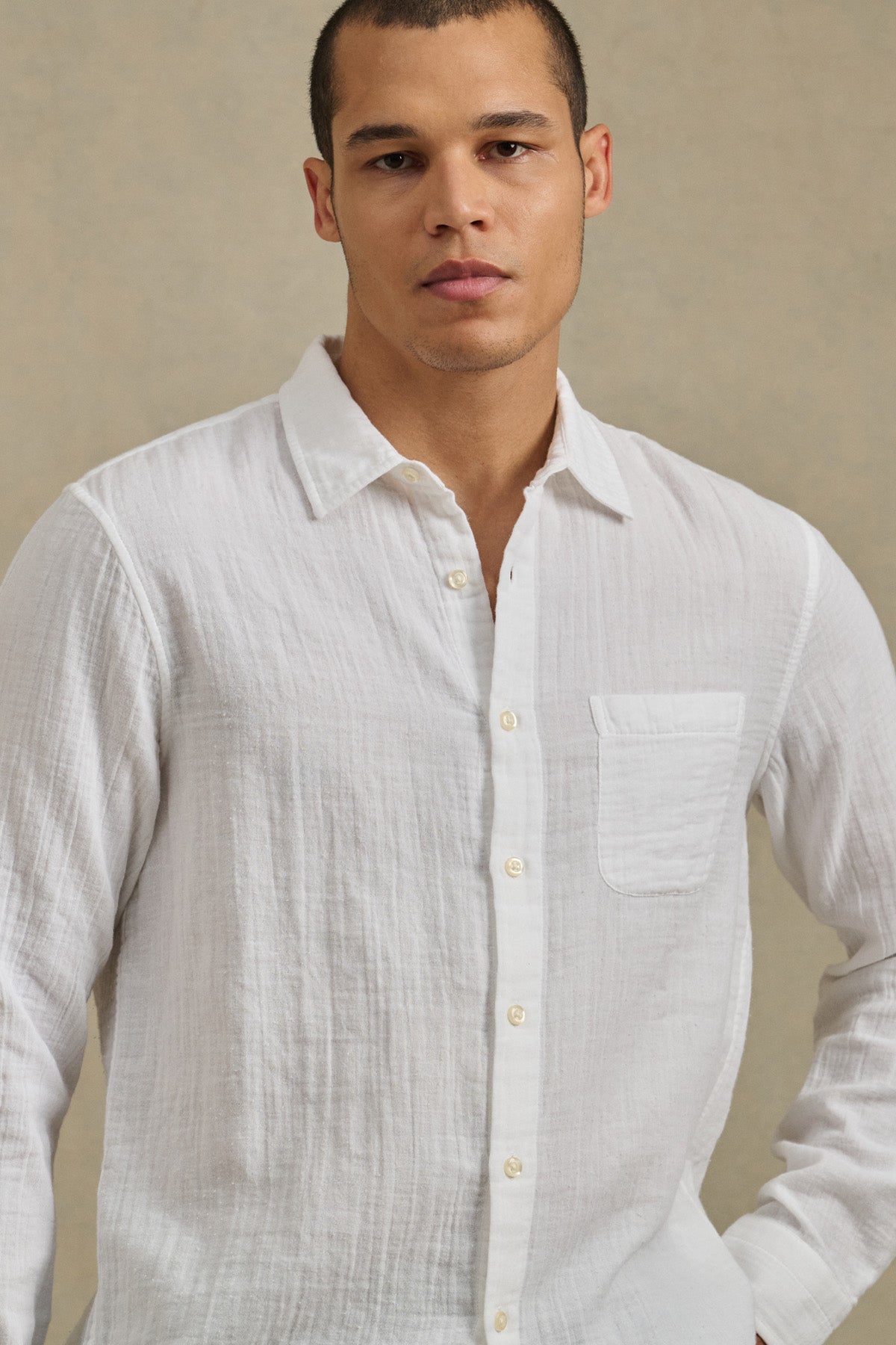 A man wearing the APOLLO SHIRT by Velvet by Graham & Spencer, a white classic-collar button-up crafted from lightweight cotton gauze, stands against a neutral background.-41297073864897