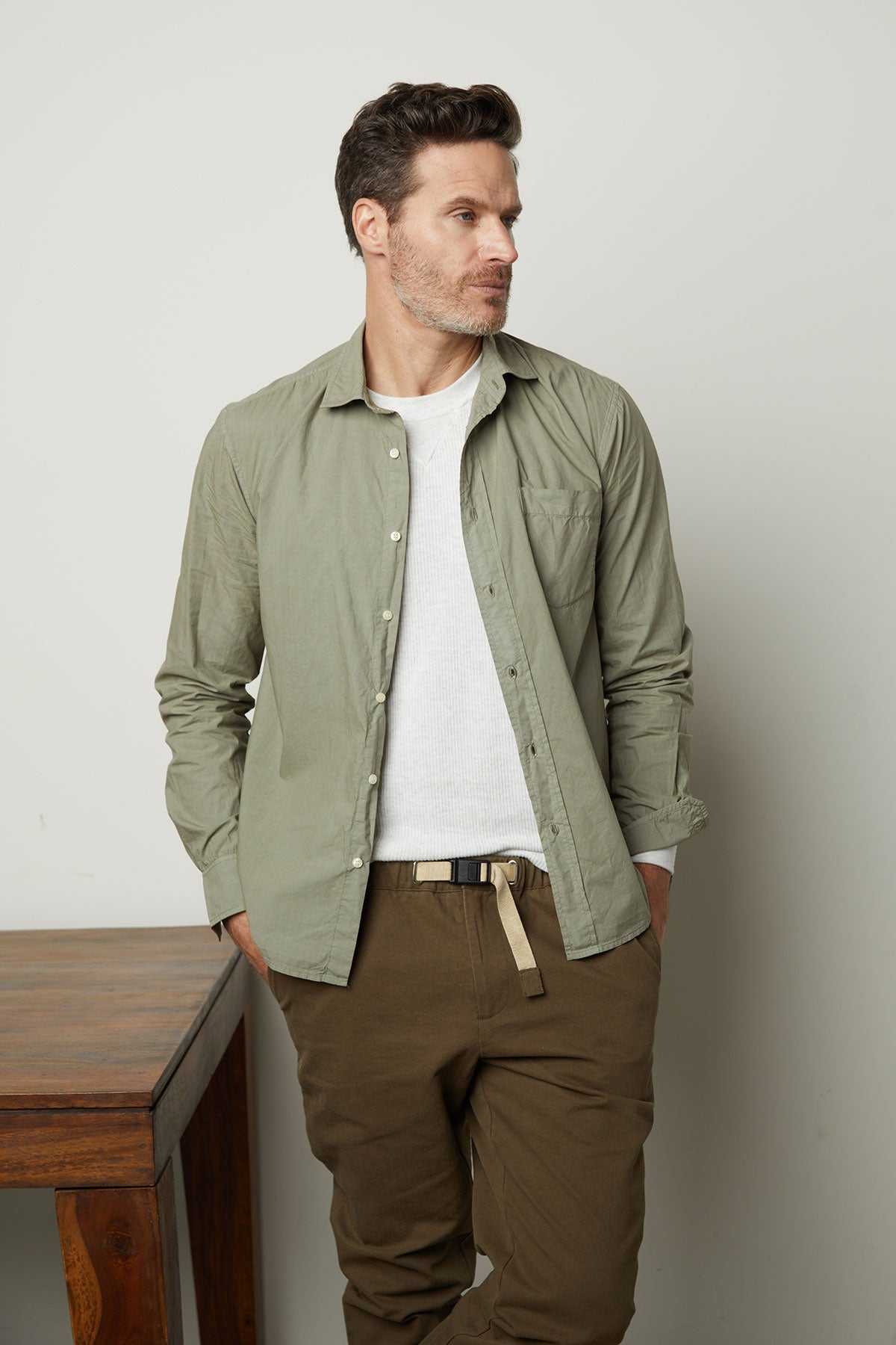 A man in the Velvet by Graham & Spencer AUGUSTUS RIB KNIT CREW shirt and khaki pants, leaning against a table, exuding unparalleled comfort.-35678459691201