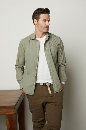 A man in the Velvet by Graham & Spencer AUGUSTUS RIB KNIT CREW shirt and khaki pants, leaning against a table, exuding unparalleled comfort.