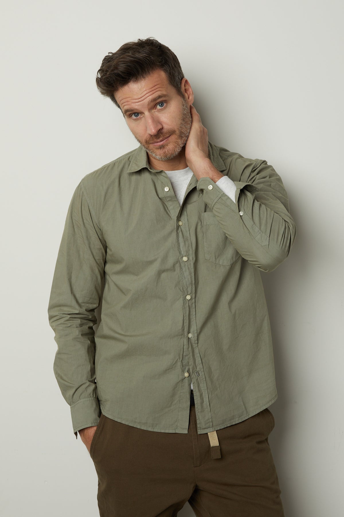 A man in a BROOKS BUTTON-UP SHIRT by Velvet by Graham & Spencer leaning against a wall.-35782370164929