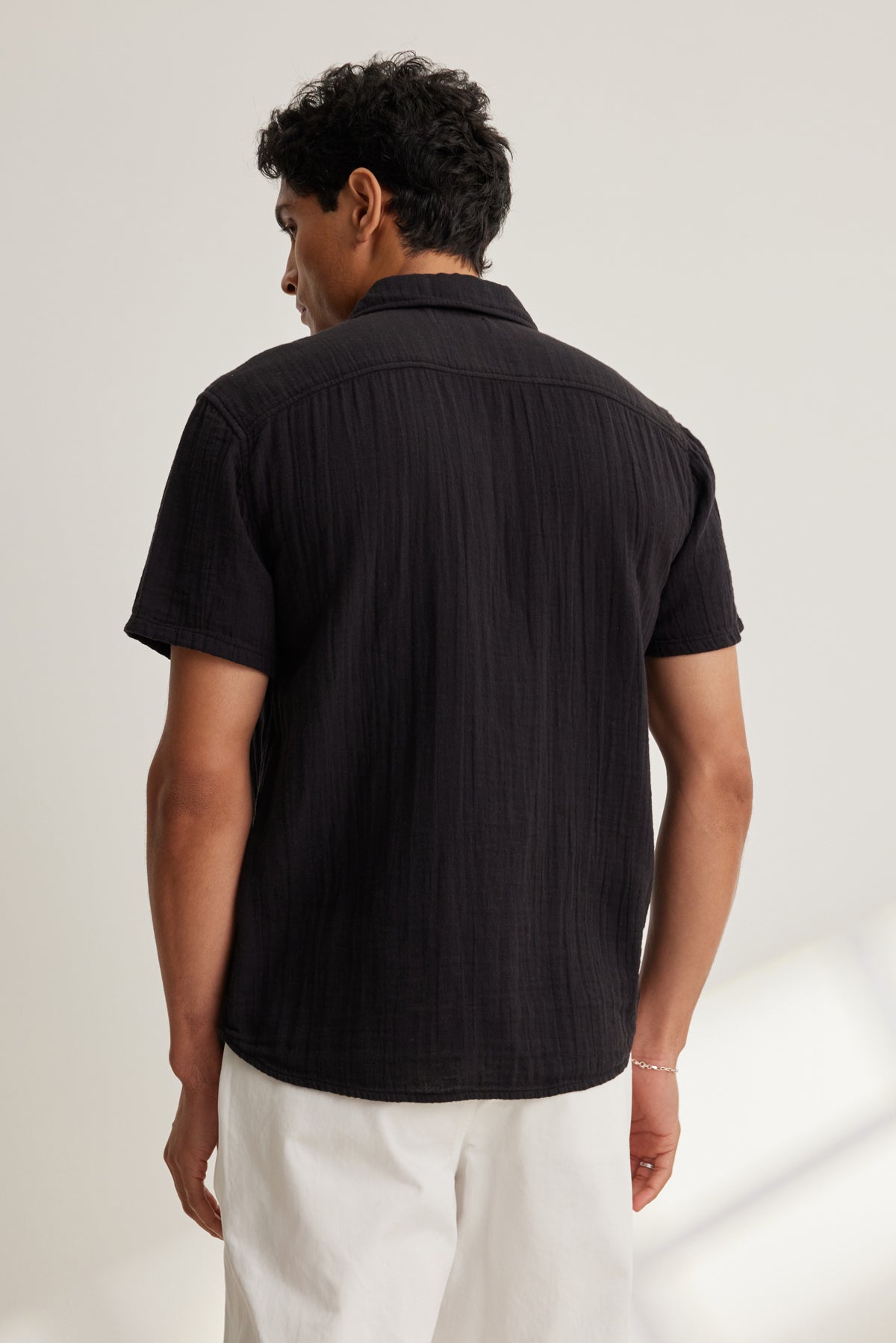   A man stands with his back to the camera against a neutral background, wearing the Velvet by Graham & Spencer CHRISTIAN COTTON GAUZE BUTTON-UP SHIRT in black and white pants. 
