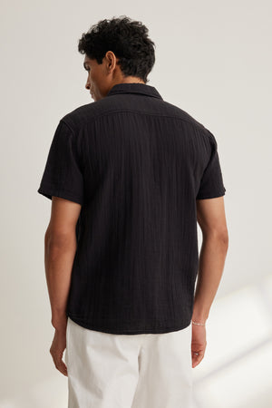 A man stands with his back to the camera against a neutral background, wearing the Velvet by Graham & Spencer CHRISTIAN COTTON GAUZE BUTTON-UP SHIRT in black and white pants.