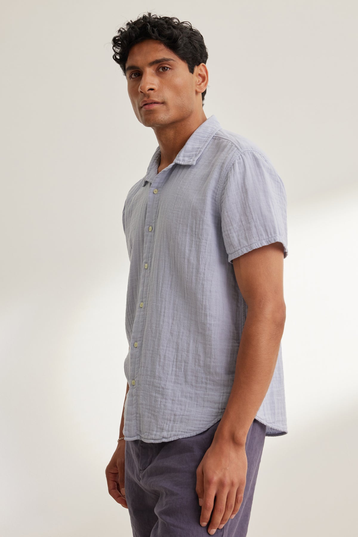 A man models the CHRISTIAN COTTON GAUZE BUTTON-UP SHIRT by Velvet by Graham & Spencer in light purple with dark pants, standing against a plain light background and facing slightly to the side.-39152371433665